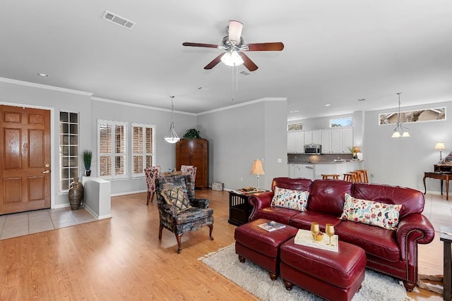 living area featuring light wood-style floors, baseboards, visible vents, and ornamental molding