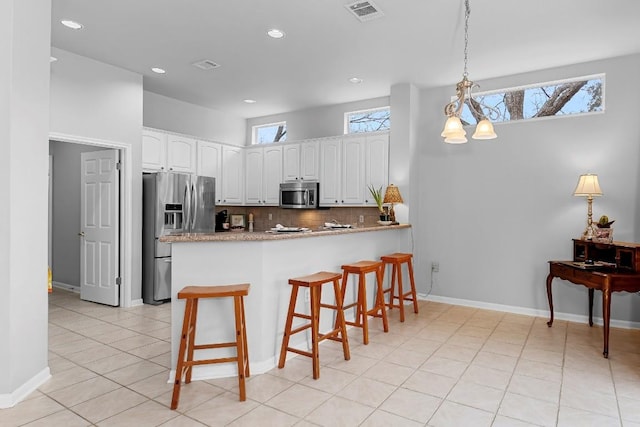 kitchen with pendant lighting, stainless steel appliances, visible vents, white cabinetry, and a peninsula