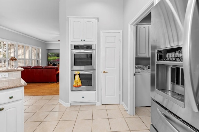 kitchen with washing machine and clothes dryer, white cabinetry, stainless steel appliances, and light tile patterned flooring