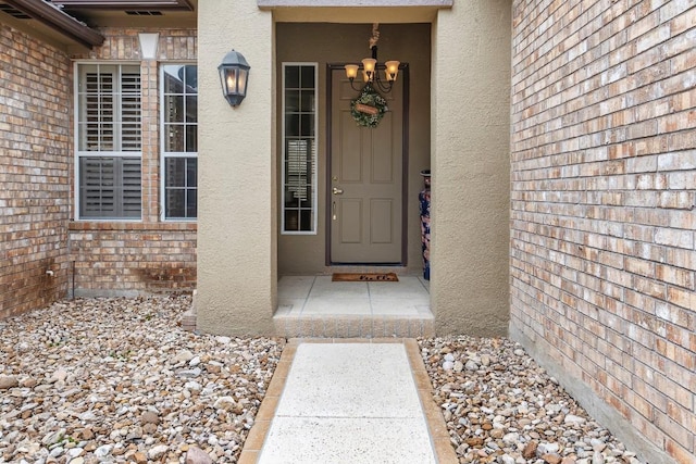 view of exterior entry with stucco siding and brick siding