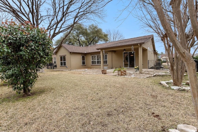 rear view of house with a yard, ceiling fan, fence, and stucco siding