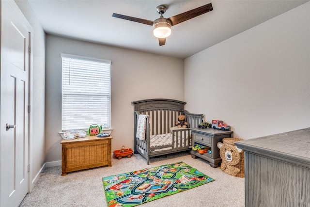 bedroom with a ceiling fan, a nursery area, and light carpet