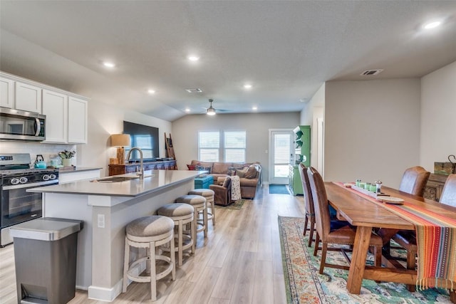 kitchen featuring white cabinets, appliances with stainless steel finishes, open floor plan, a kitchen island with sink, and a sink