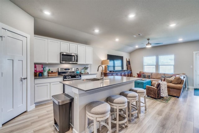 kitchen with a kitchen island with sink, a sink, white cabinetry, open floor plan, and appliances with stainless steel finishes