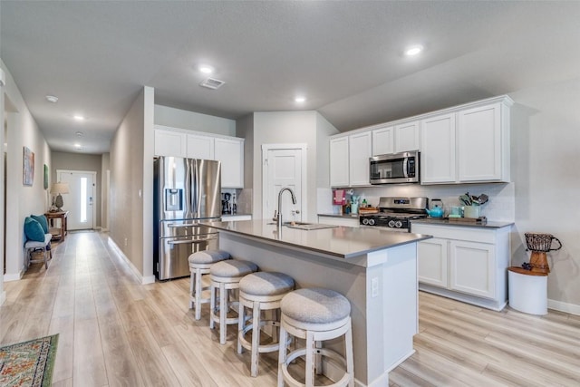 kitchen featuring appliances with stainless steel finishes, white cabinetry, a sink, and a center island with sink