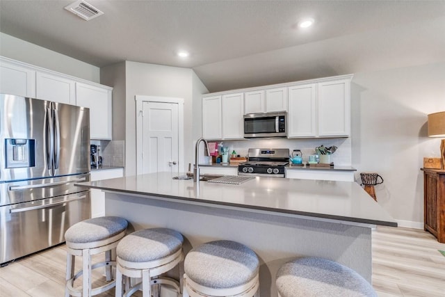 kitchen featuring stainless steel appliances, visible vents, white cabinetry, decorative backsplash, and a center island with sink