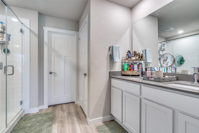 full bath featuring double vanity, a stall shower, a sink, and wood finished floors