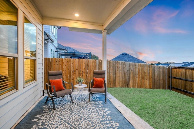 patio terrace at dusk featuring a fenced backyard and a yard