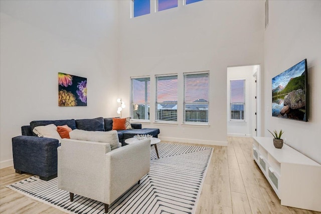 living room featuring a towering ceiling, light wood-style flooring, and baseboards