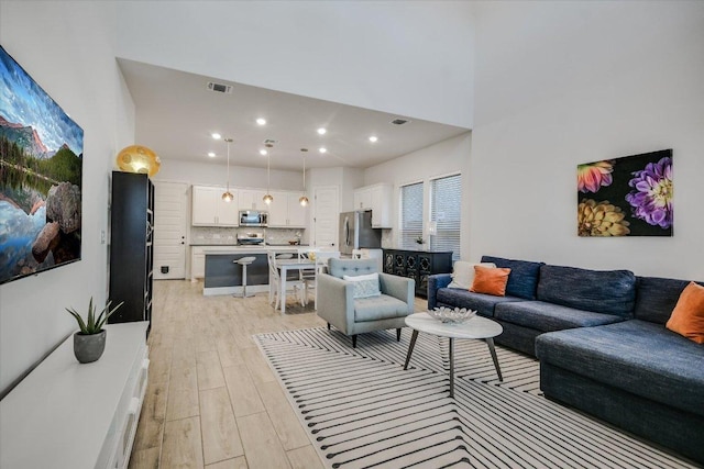 living room featuring recessed lighting, a towering ceiling, visible vents, and light wood-style floors