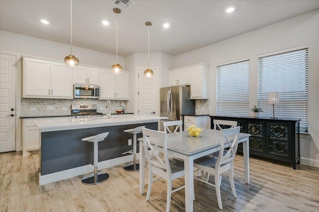 kitchen with stainless steel appliances, white cabinetry, light countertops, an island with sink, and pendant lighting