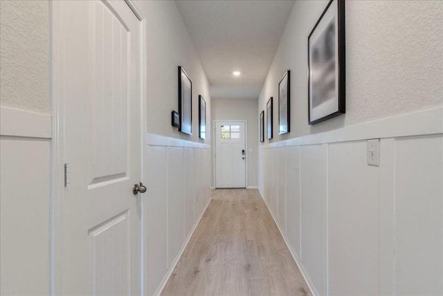 hallway featuring light wood-style flooring, a wainscoted wall, a decorative wall, and recessed lighting