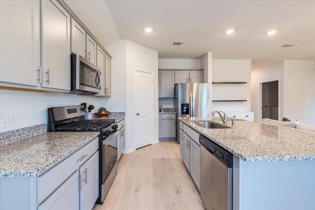 kitchen with appliances with stainless steel finishes, a sink, gray cabinetry, light wood-type flooring, and a center island with sink