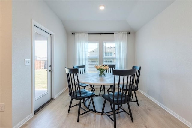 dining area featuring light wood-style flooring, baseboards, and vaulted ceiling