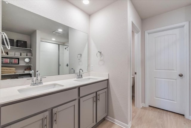 bathroom with wood finished floors, double vanity, a shower stall, toilet, and recessed lighting