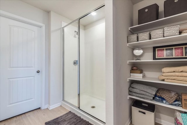 full bathroom with wood finished floors, a stall shower, and baseboards