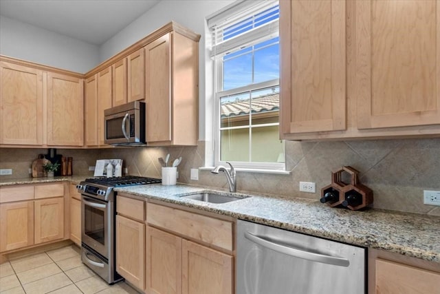 kitchen with light stone counters, a sink, appliances with stainless steel finishes, backsplash, and light brown cabinetry