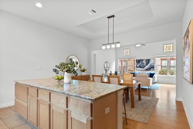 kitchen featuring open floor plan, a kitchen island, a raised ceiling, and pendant lighting