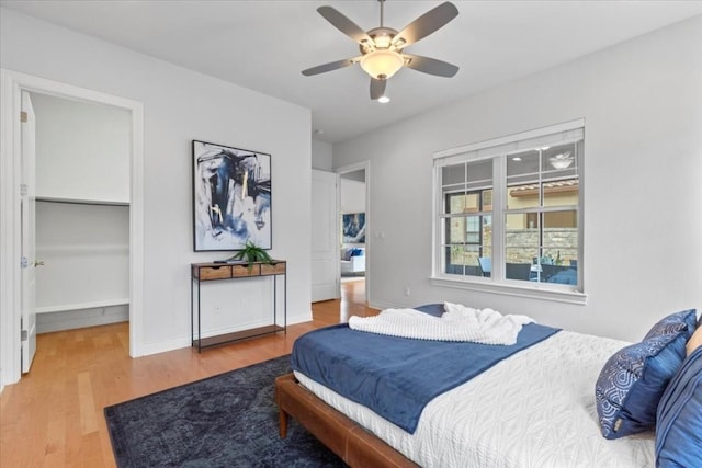 bedroom featuring ceiling fan, a spacious closet, baseboards, and wood finished floors