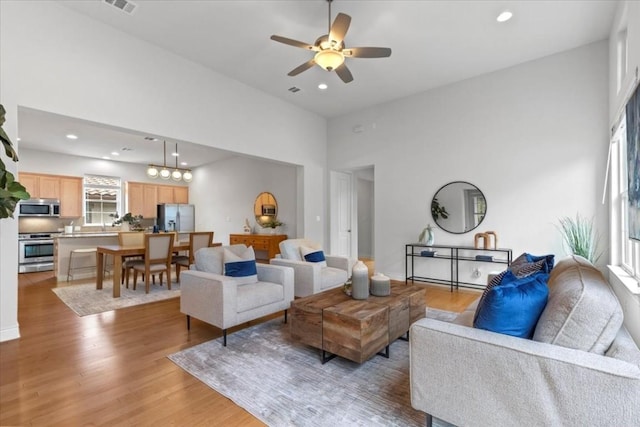 living area featuring a ceiling fan, light wood-type flooring, a towering ceiling, and recessed lighting