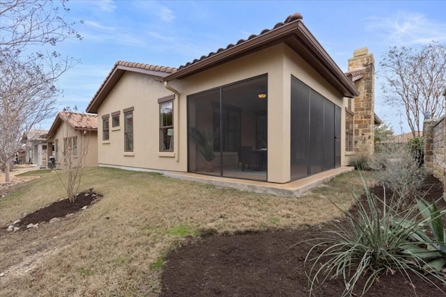 back of property with a sunroom, a chimney, a lawn, and stucco siding