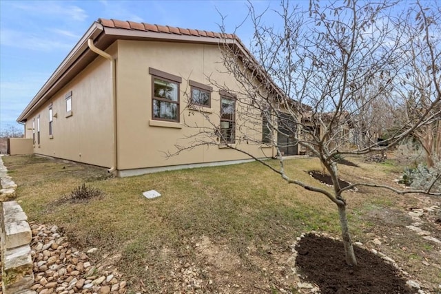 view of side of home with a tile roof, a lawn, and stucco siding