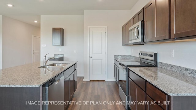 kitchen featuring light stone counters, stainless steel appliances, a sink, dark brown cabinets, and dark wood finished floors