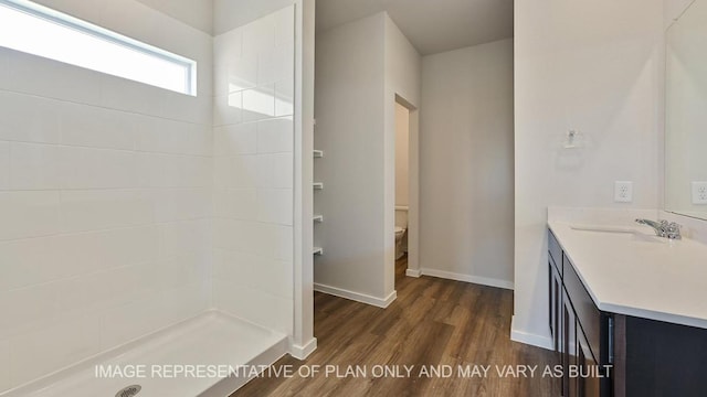 bathroom featuring baseboards, tiled shower, toilet, wood finished floors, and vanity