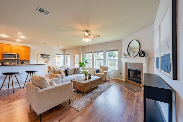 living room featuring a tile fireplace, visible vents, baseboards, a ceiling fan, and light wood-type flooring