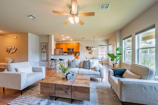 living room featuring ceiling fan with notable chandelier, wood finished floors, visible vents, and baseboards