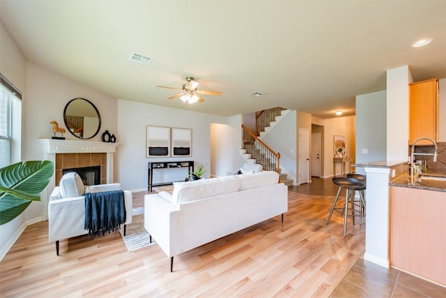 living area with a tile fireplace, visible vents, baseboards, stairway, and light wood-type flooring