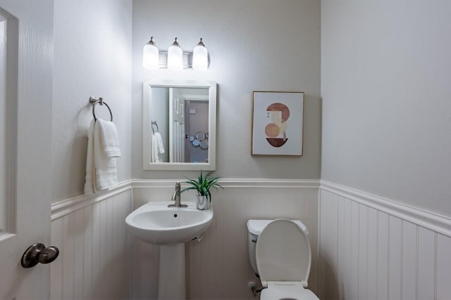 half bathroom featuring a wainscoted wall, a sink, and toilet