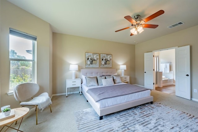 bedroom with ceiling fan, ensuite bathroom, light colored carpet, visible vents, and baseboards