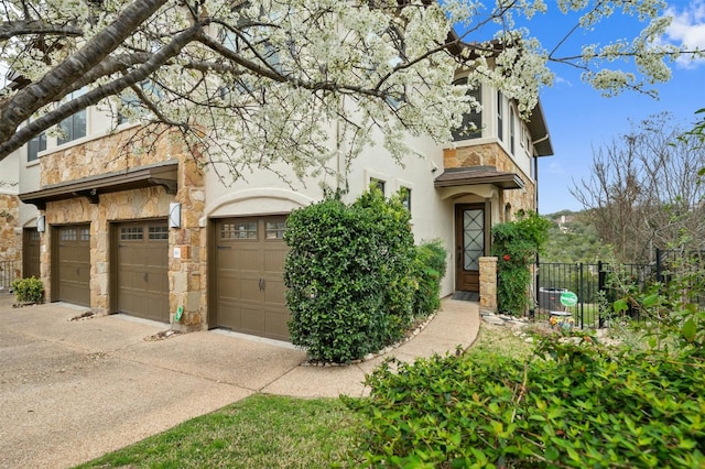 view of front of house with a garage, concrete driveway, stone siding, fence, and stucco siding