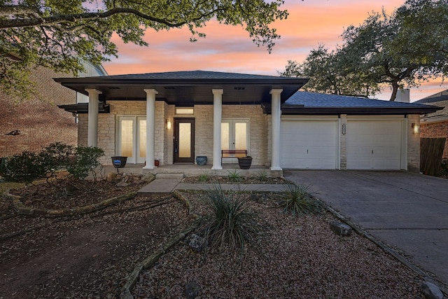 view of front of house featuring a garage, covered porch, a shingled roof, stone siding, and concrete driveway