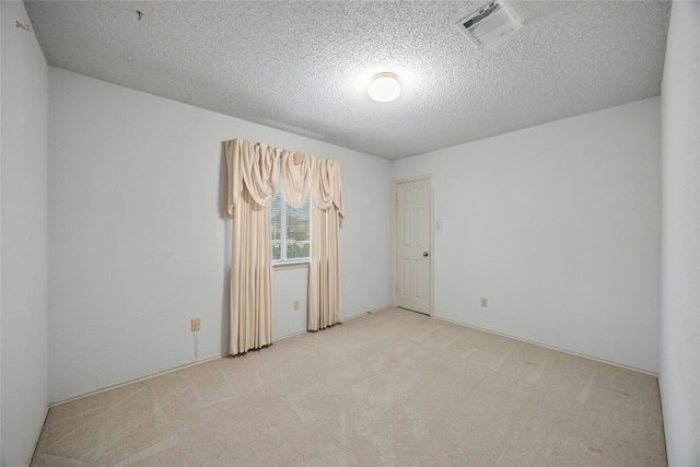 spare room featuring light carpet, visible vents, and a textured ceiling