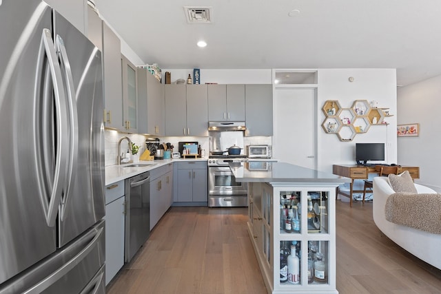 kitchen with gray cabinetry, under cabinet range hood, dark wood-type flooring, stainless steel appliances, and a sink