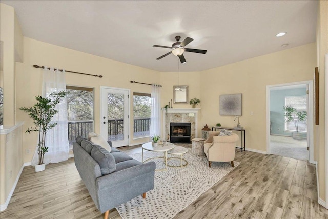 living room with a ceiling fan, a healthy amount of sunlight, a fireplace, and light wood finished floors