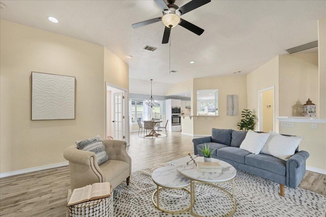 living area featuring ceiling fan with notable chandelier, light wood-type flooring, visible vents, and baseboards