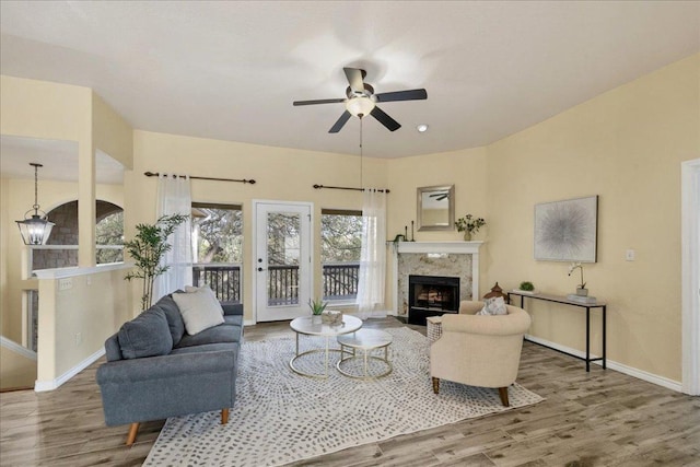 living area featuring ceiling fan, baseboards, wood finished floors, and a high end fireplace