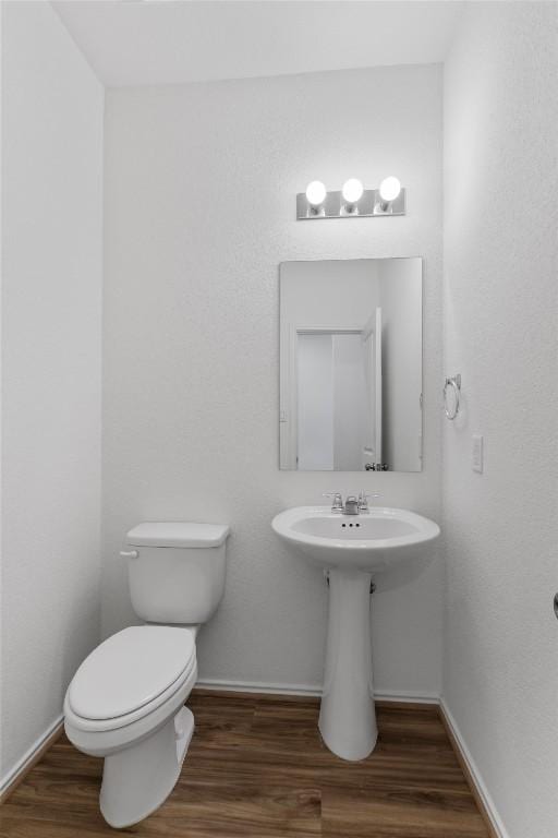 half bathroom featuring toilet, baseboards, and wood finished floors