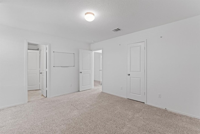 spare room featuring light carpet, baseboards, visible vents, and a textured ceiling