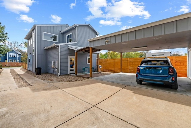 exterior space with a carport, board and batten siding, concrete driveway, and fence