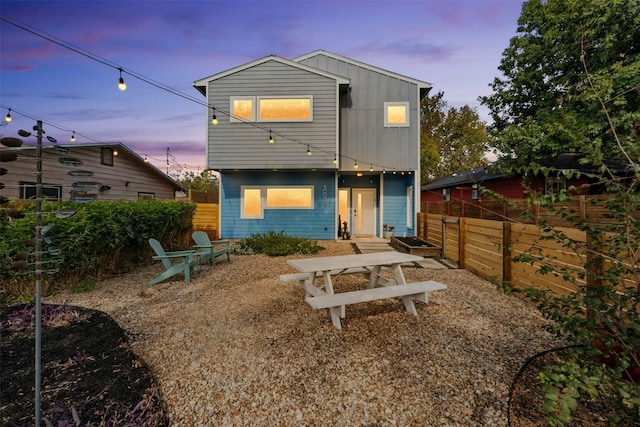 back of property at dusk featuring board and batten siding and fence