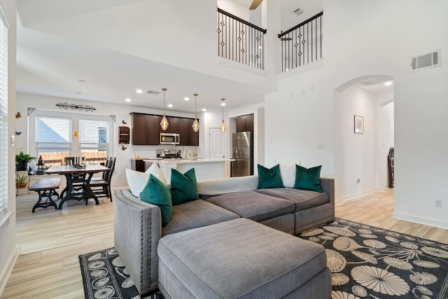 living area featuring arched walkways, visible vents, a high ceiling, light wood-type flooring, and baseboards