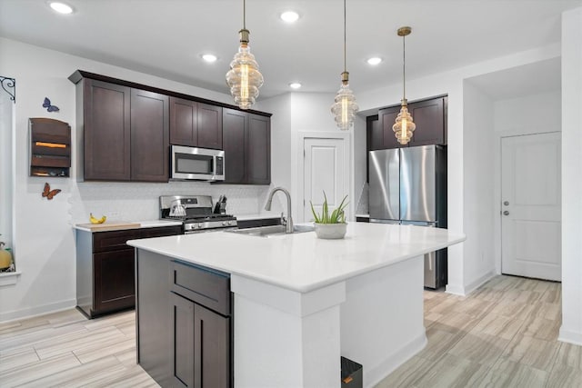 kitchen with appliances with stainless steel finishes, a kitchen island with sink, light countertops, pendant lighting, and a sink