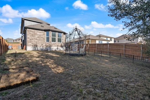 back of property with a trampoline, brick siding, a yard, a residential view, and a fenced backyard