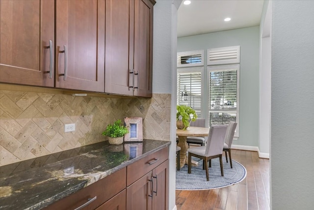 kitchen with wood finished floors, baseboards, brown cabinets, tasteful backsplash, and dark stone countertops