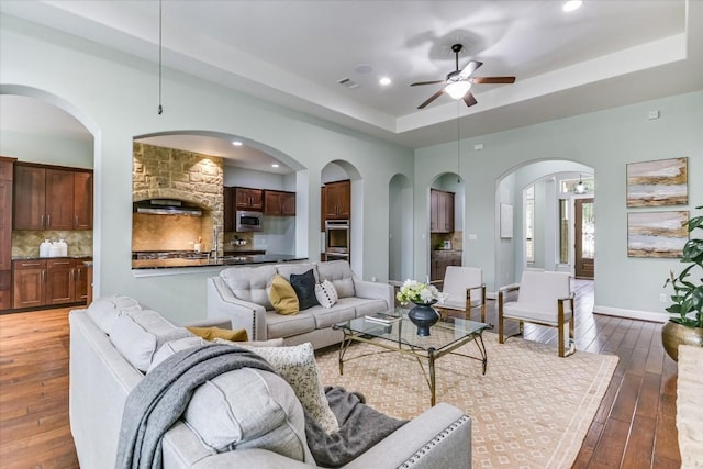 living area with a tray ceiling, recessed lighting, visible vents, dark wood-type flooring, and ceiling fan