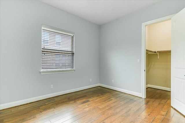 unfurnished bedroom featuring light wood-type flooring, baseboards, a walk in closet, and a closet